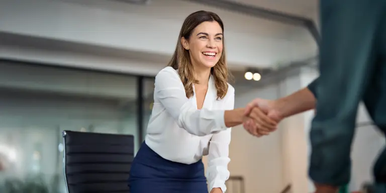 Geschäftsfrau lächelt und gibt einem Kunden im Büro die Hand.