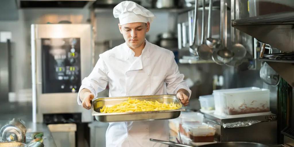 Koch in weißer Uniform hält Tablett mit Rohkost in einer professionellen Restaurantküche.